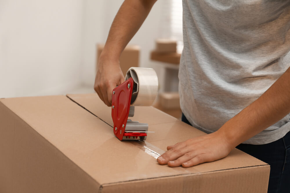 A person sealing a box with packing tape while moving