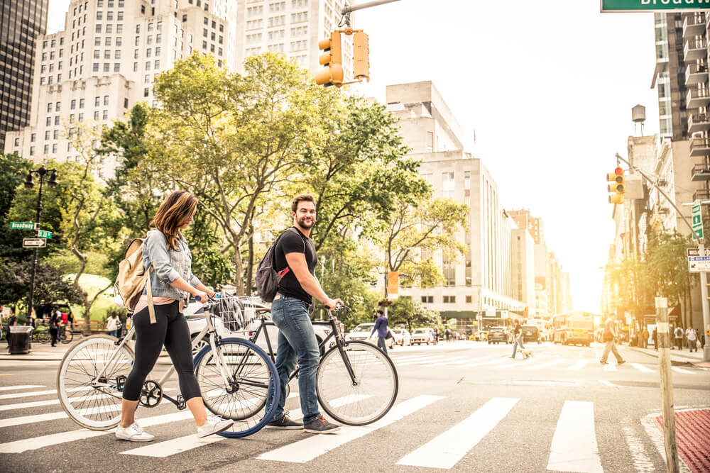 A couple crossing the street with their bikes.