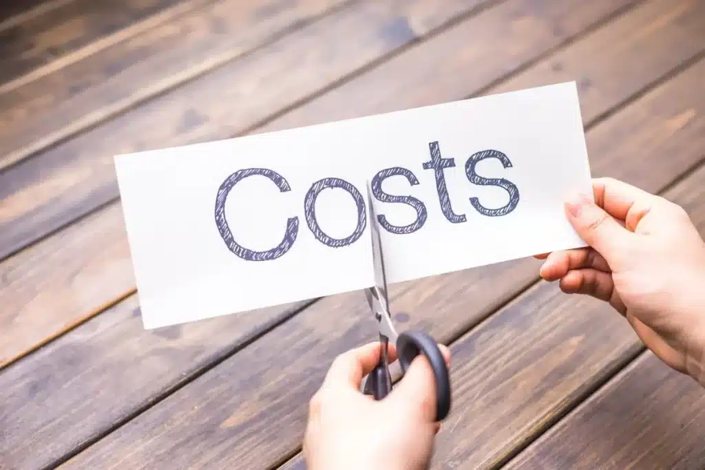 Hands using scissors to cut a paper sign that reads Costs